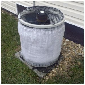 Outdoor air conditioner condenser unit with heavy ice buildup around the housing, sitting on a concrete pad beside a house.